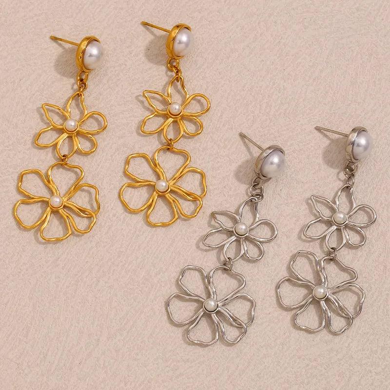 Pair of gold and silver floral earrings with pearl centers on a beige background