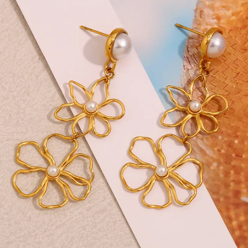 Gold floral earrings with pearl centers on a textured surface