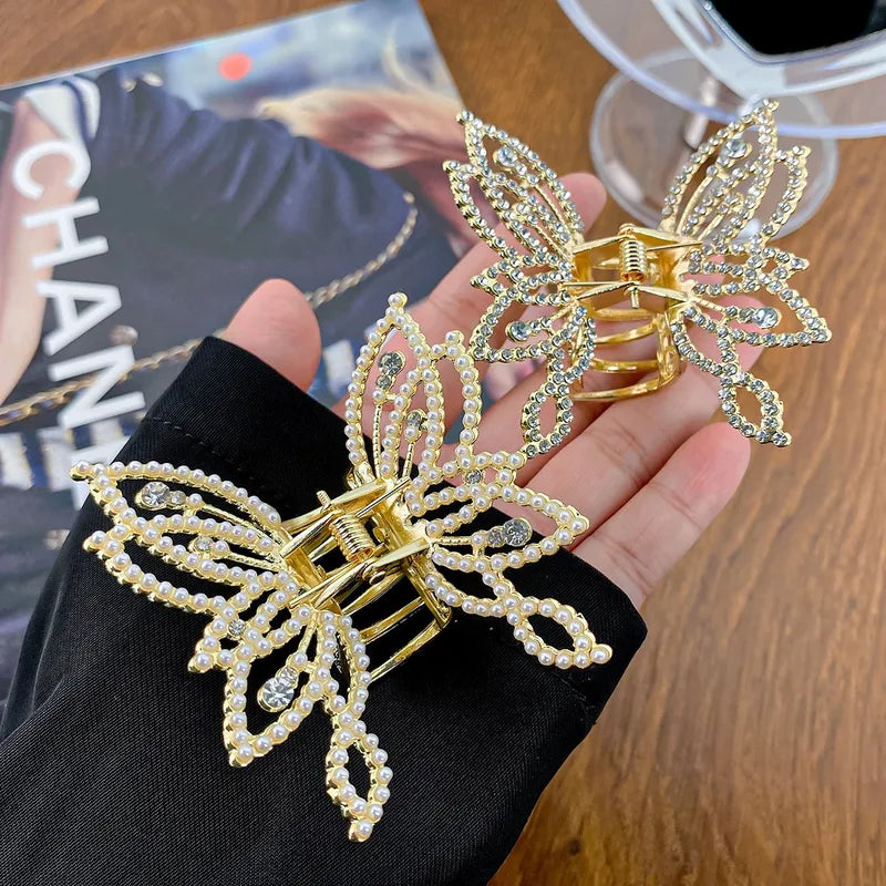 Gold butterfly hair clips with rhinestones held by a hand on a wooden surface.