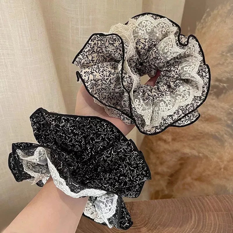 Two lace scrunchies, one black and white patterned and one solid black, held against a neutral background.
