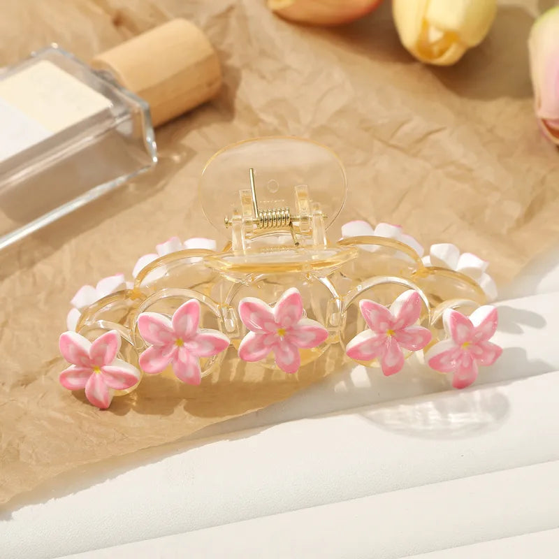Clear hair clip with pink floral decorations on a light brown surface