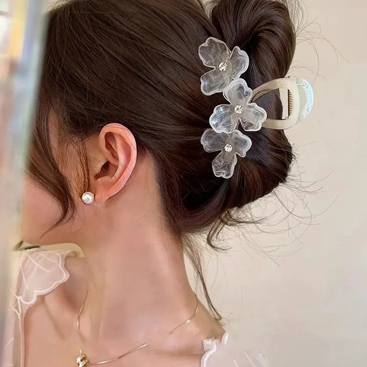 Woman with floral hair clip and pearl earrings against a neutral background