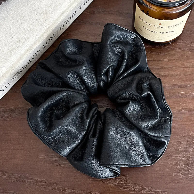 Black scrunchie on a wooden surface with a book and jar in the background