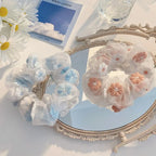 Two floral hair scrunchies on a decorative mirror with a blue sky background.