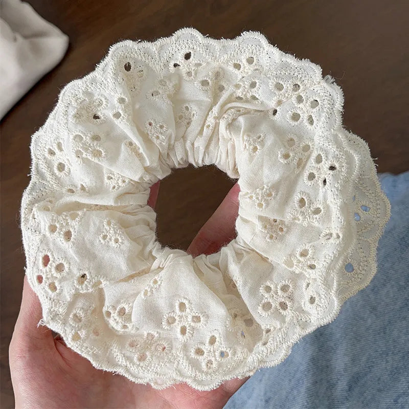 White lace scrunchie held in a hand with a blurred background
