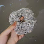 Silver scrunchie held by a hand with a dark background