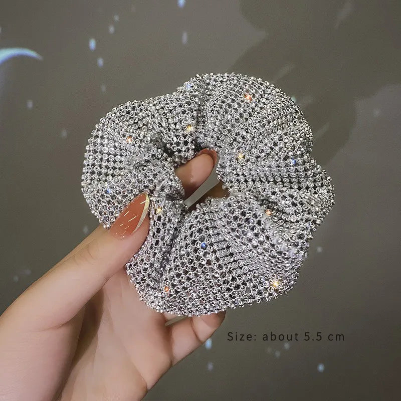 Silver scrunchie held by a hand with a dark background