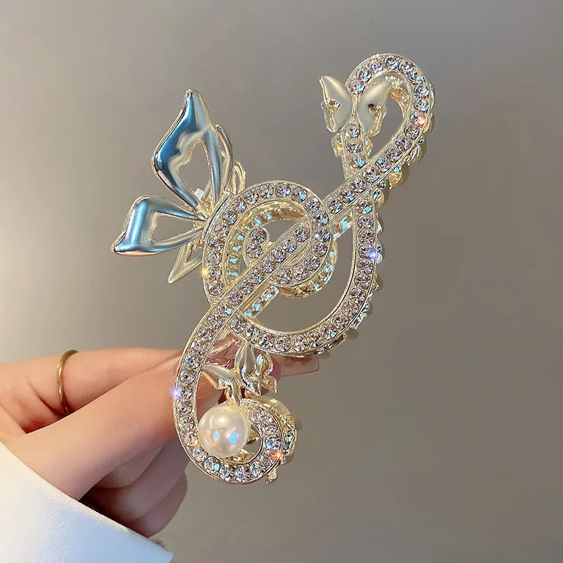 Decorative clip with musical notes and pearl held by a hand against a neutral background