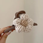 Knitted flower-shaped hair scrunchie with brown handles held by a hand against a plain background
