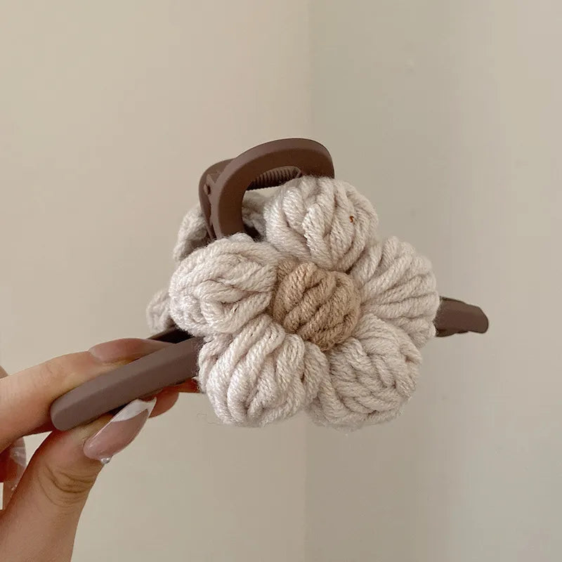 Knitted flower-shaped hair scrunchie with brown handles held by a hand against a plain background
