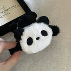 Panda-shaped plush scrunchies held by a hand on a textured surface