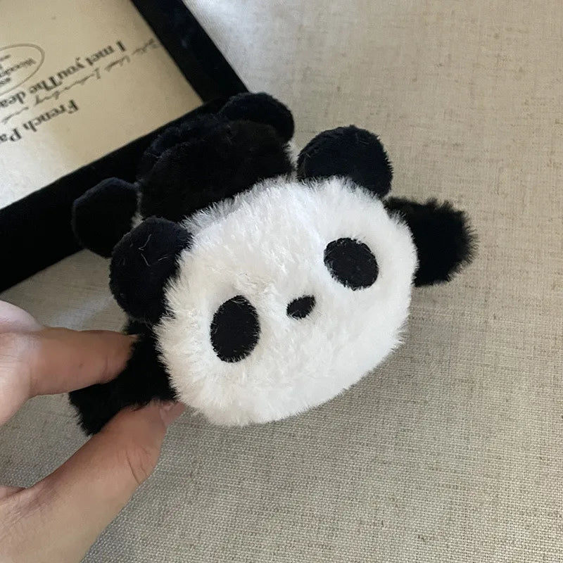 Panda-shaped plush scrunchies held by a hand on a textured surface