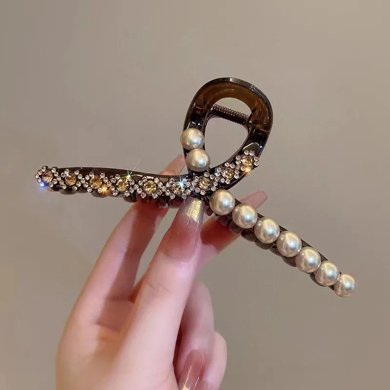 Hand holding a decorative hair clip with pearls and crystals against a neutral background