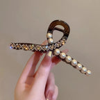 Hand holding a decorative hair clip with pearls and crystals against a neutral background