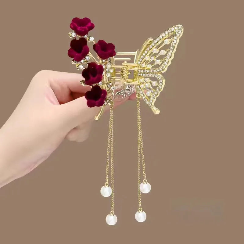 Decorative hair clip with red flowers and gold butterfly design held by a hand on a brown background