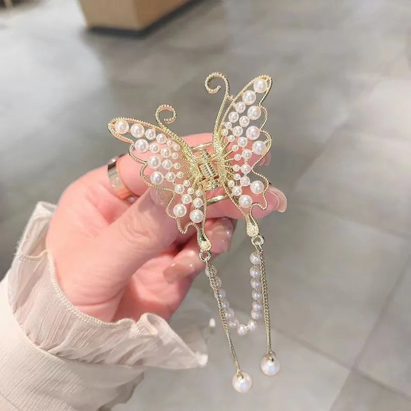 Butterfly shaped hair claw with pearls held by a hand on a neutral background