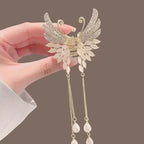 Decorative hair accessory with angel wings held by a hand against a brown background