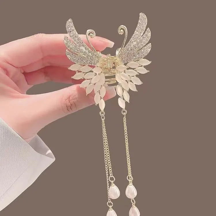 Decorative hair accessory with angel wings held by a hand against a brown background