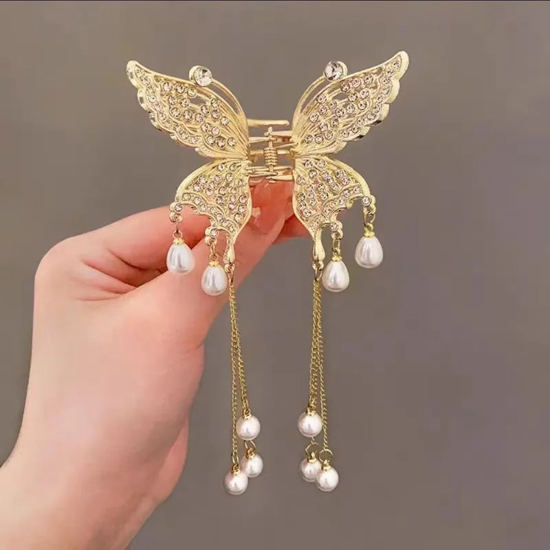 Gold butterfly hair clip with pearl decorations held by a hand against a neutral background