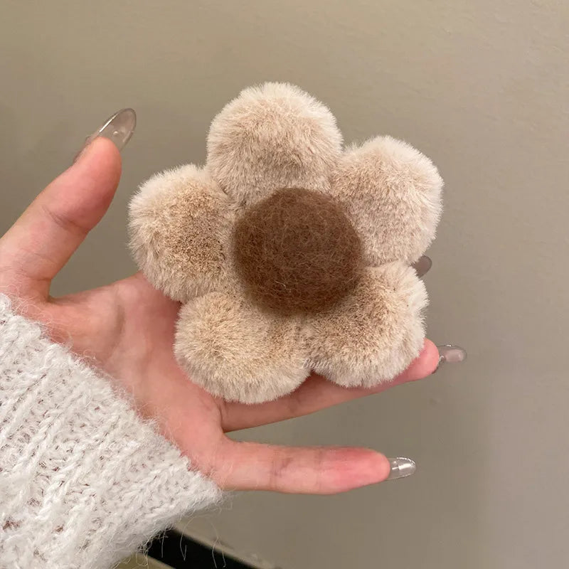 Hand holding a fluffy flower-shaped clipt with a brown center against a plain background