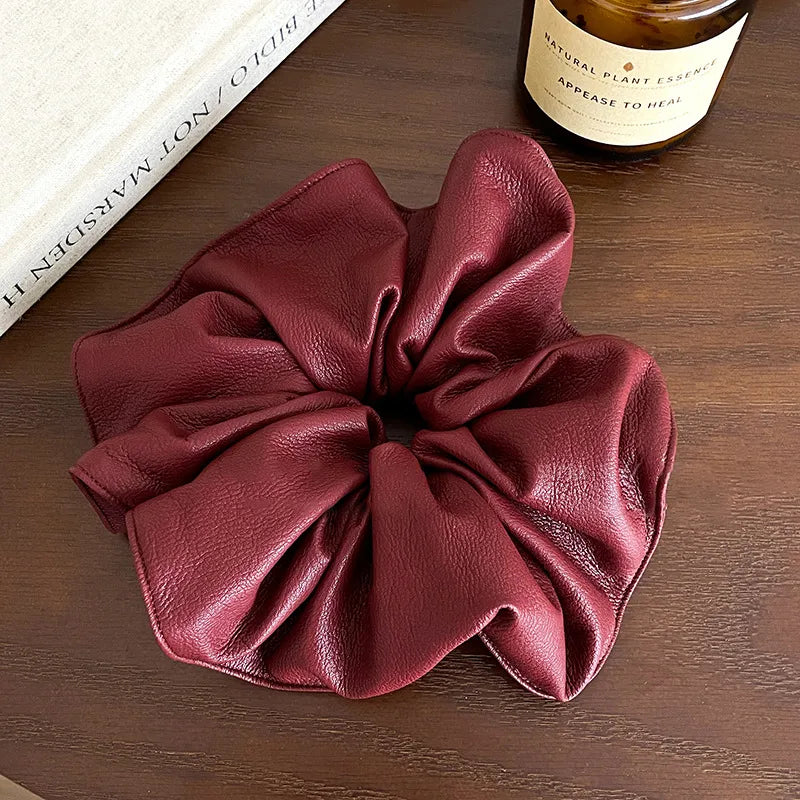 Red leather scrunchie on a wooden surface with a bottle of essential oil in the background.
