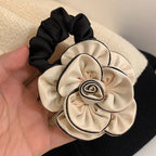 Black scrunchie and cream flower-shaped hair accessory held by a hand against a neutral background