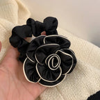 Black scrunchie with floral design held in a hand against a neutral background