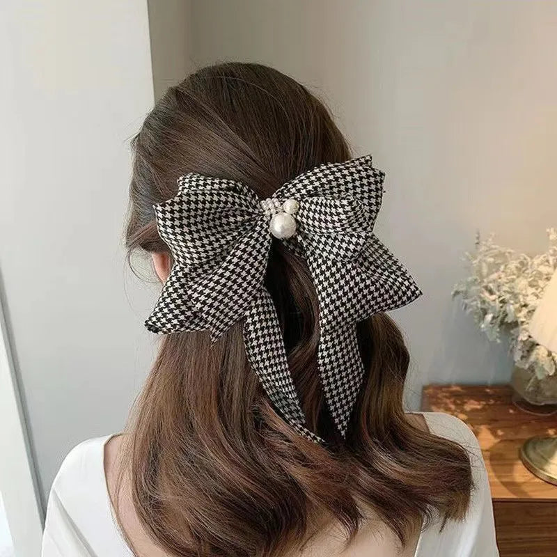 Person with a large black and white checkered hair bow in their hair, indoors.