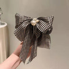 Black and white checkered bow with pearls held by a hand against a neutral background