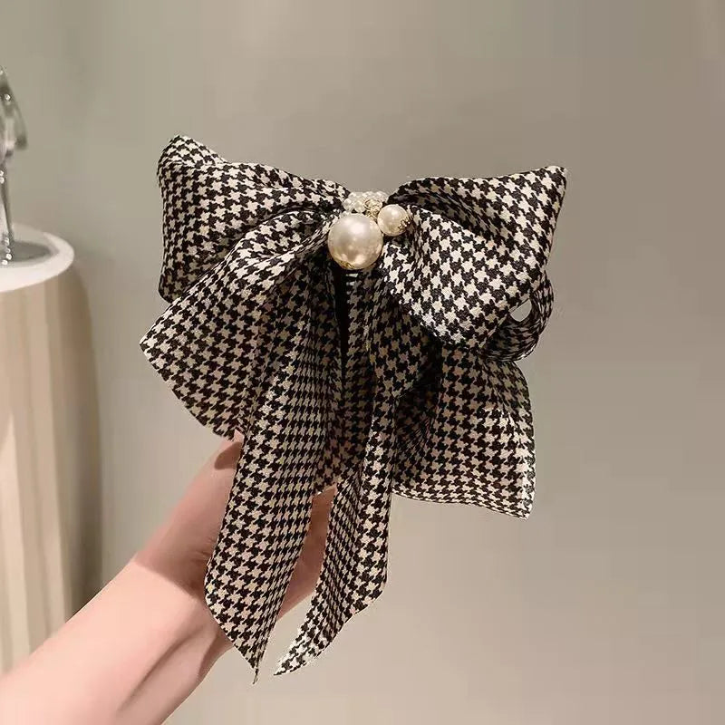 Black and white checkered bow with pearls held by a hand against a neutral background