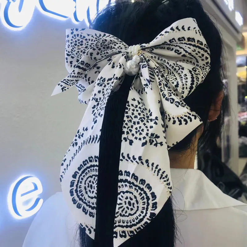 Person wearing a large black and white patterned bow headband with a blurred background.