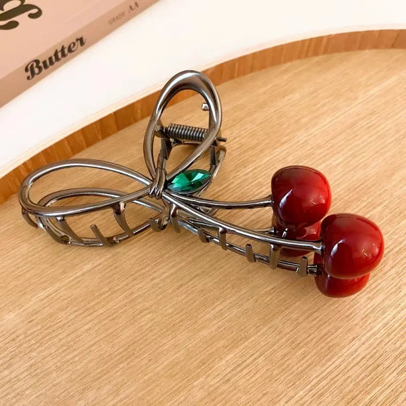 Metallic hair roller with red cherry-like ends on a wooden surface