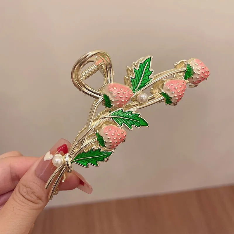 Decorative hair clip with strawberry design held by a hand against a neutral background