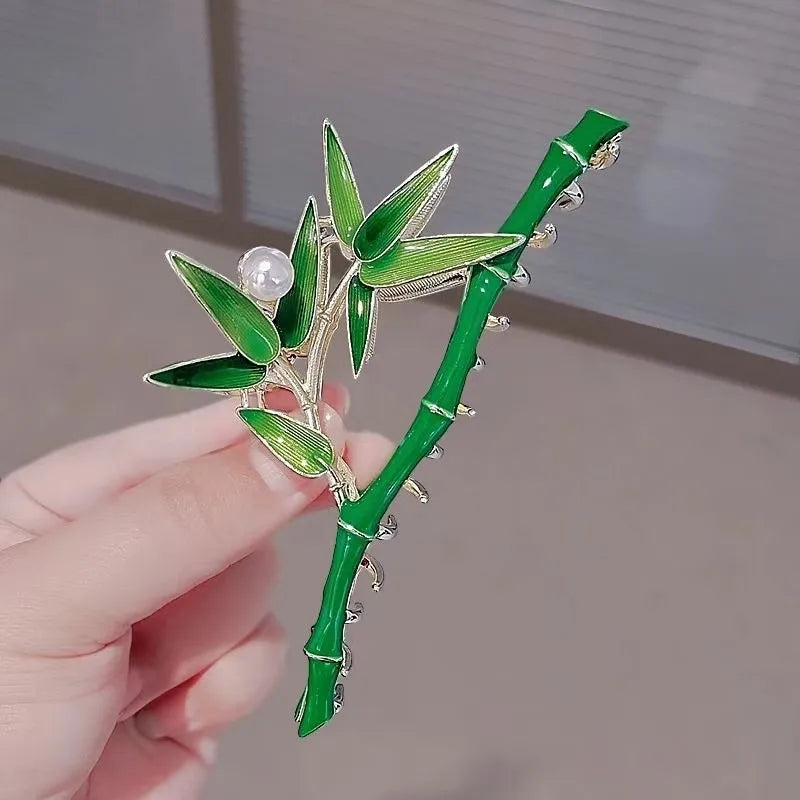 Green bamboo brooch with leaves held by a hand against a neutral background