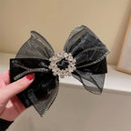 Black bow hair clip with decorative chain and central gemstone held by a hand.