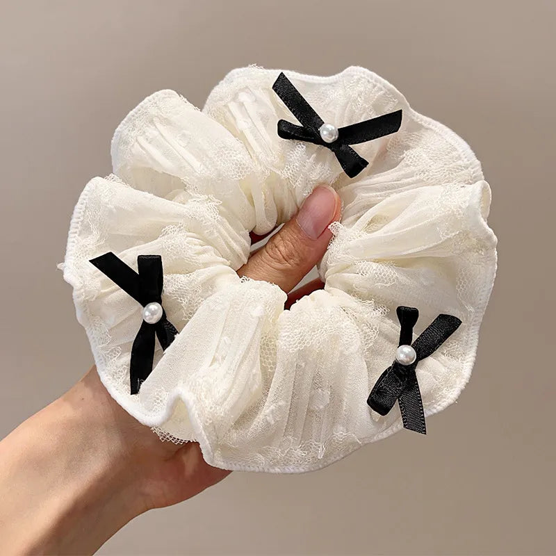 White scrunchie with black bows held by a hand against a neutral background