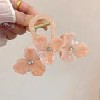 Pink floral hair clip with rhinestones held by a hand against a neutral background