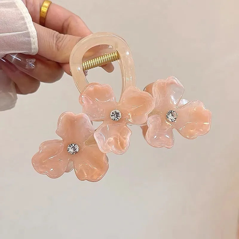 Pink floral hair clip with rhinestones held by a hand against a neutral background