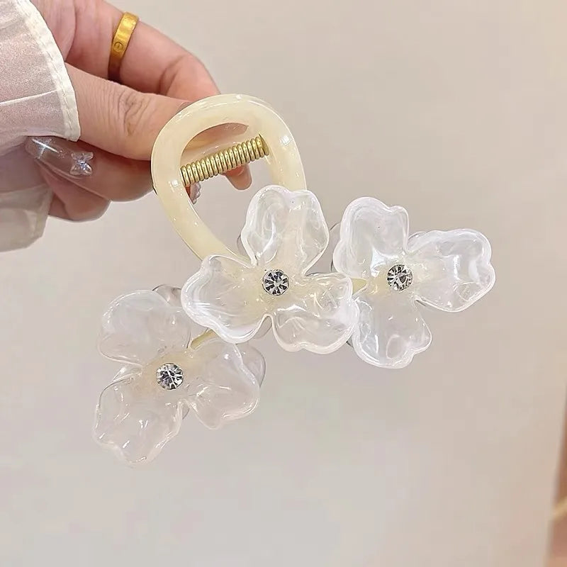 Hair scrunchie with floral design and rhinestones held by a hand against a neutral background