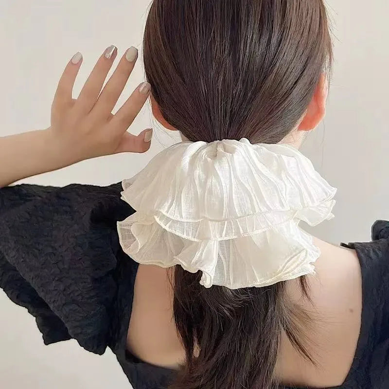 Woman wearing a white ruffled hair tie with a plain background
