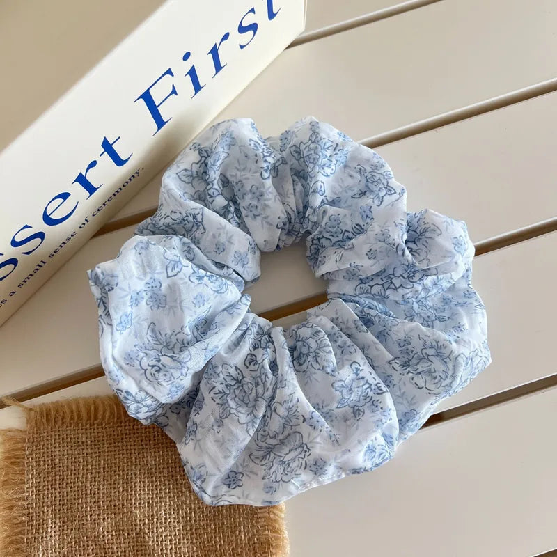 Blue floral scrunchie on a wooden surface with a book in the background
