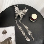 Silver butterfly hair accessory with tassels on a black surface next to a candle and photo.