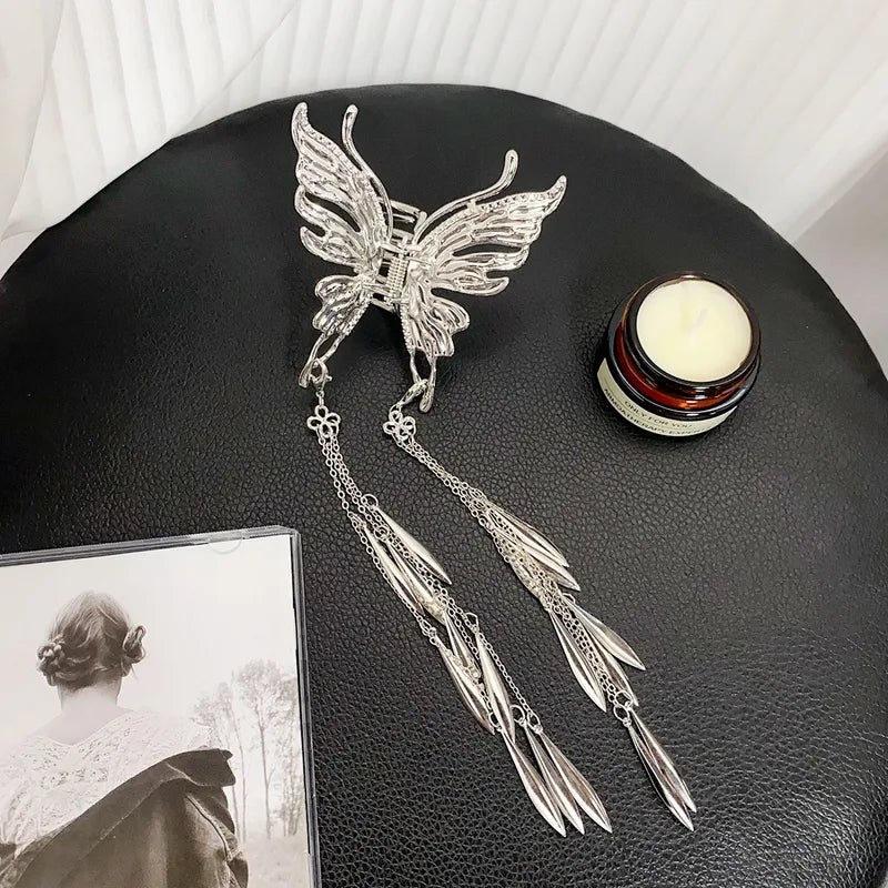 Silver butterfly hair accessory with tassels on a black surface next to a candle and photo.