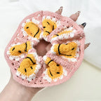 Pink crochet scrunchie with yellow faces held by a hand against a white background