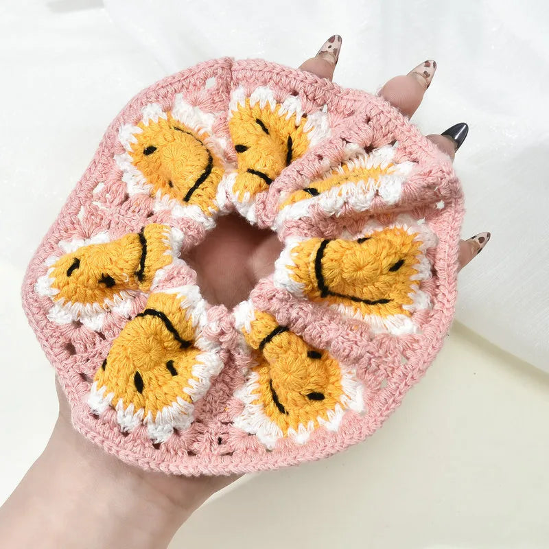 Pink crochet scrunchie with yellow faces held by a hand against a white background
