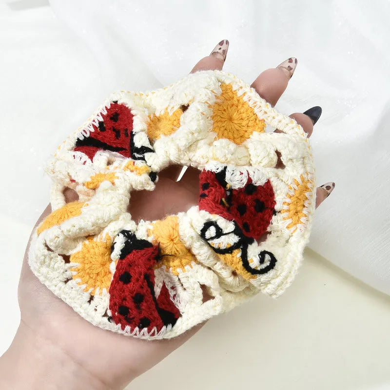 Hand holding a crocheted scrunchie with ladybug pattern on a white background