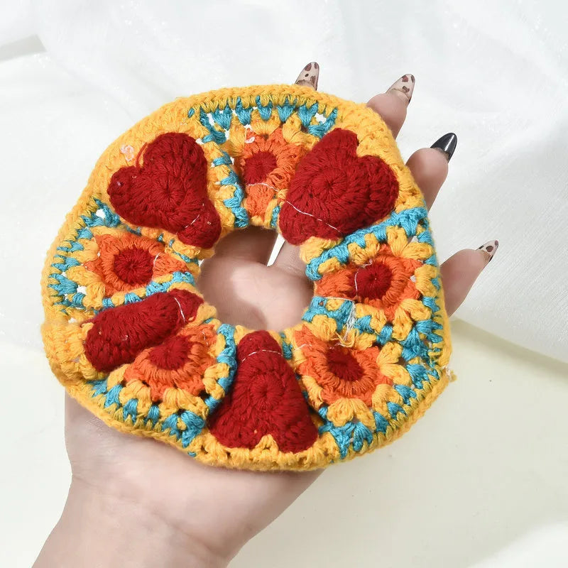 Colorful crochet heart-patterned item held by a hand with painted nails.
