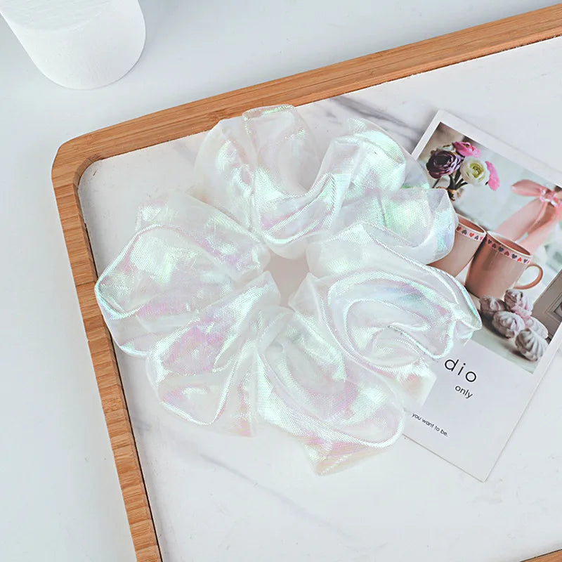 Set of three iridescent scrunchies on a wooden tray with a magazine underneath.