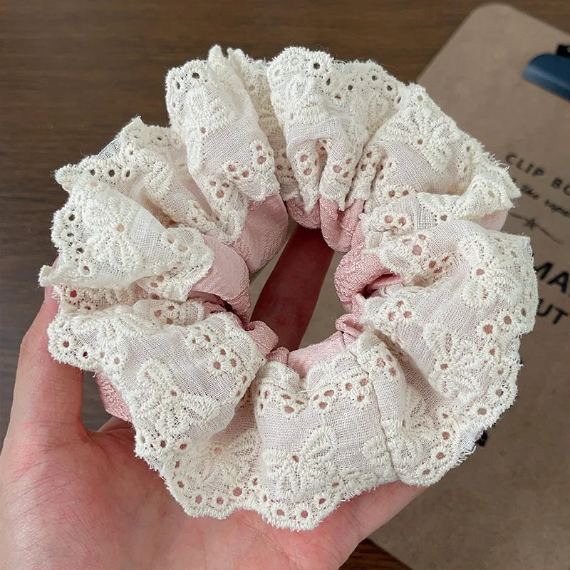 Pink scrunchie with lace details held in a hand against a blurred background