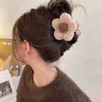 Woman with brown hair styled in an updo with a decorative flower hair accessory, wearing a brown sweater.